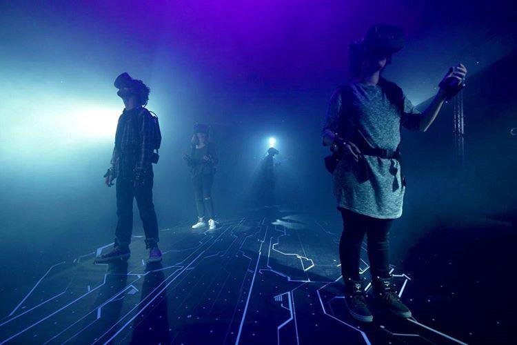 Players in VR headsets and motion-tracking gear walking on a glowing circuit floor